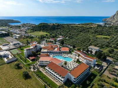 Complejo hotelero con tejados rojos y gran piscina cerca del mar y zonas verdes circundantes.
