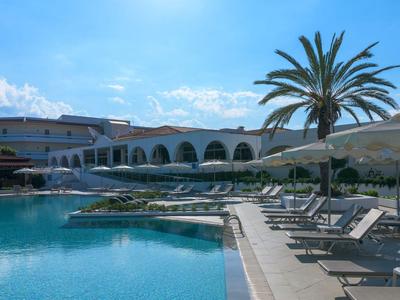 Słoneczna część basenowa z leżakami i palmami w hotelowym resorcie.