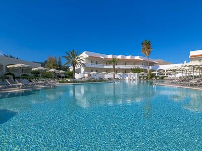 Duży basen przed białym budynkiem hotelu pod czystym niebieskim niebem