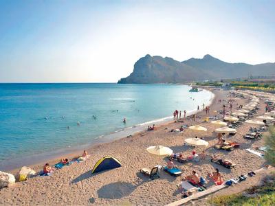 Amplia playa de arena con sombrillas y personas bajo un cielo despejado y mar tranquilo.