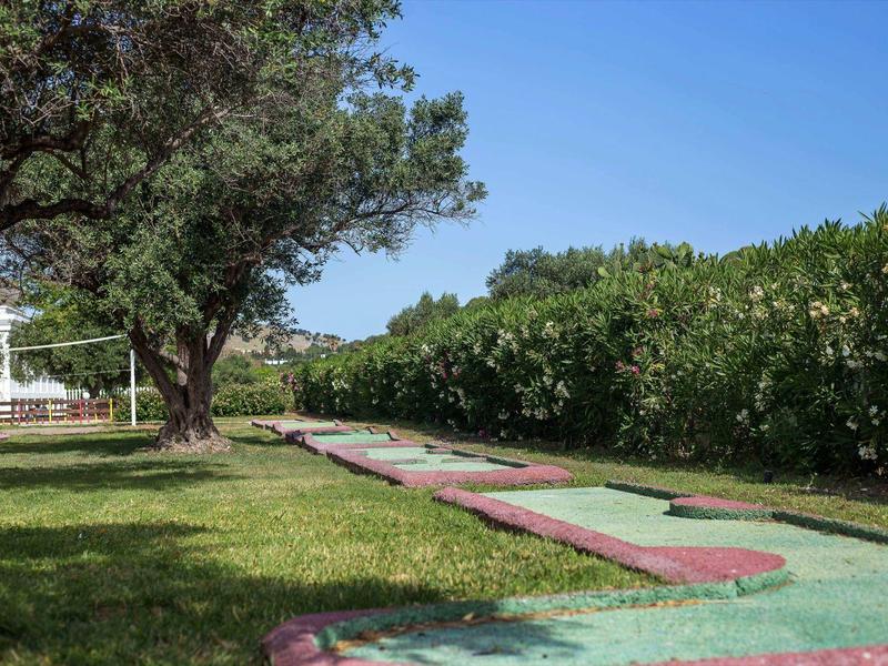Campo de minigolf con césped artificial verde y bordes rojos en el jardín bajo cielo despejado.