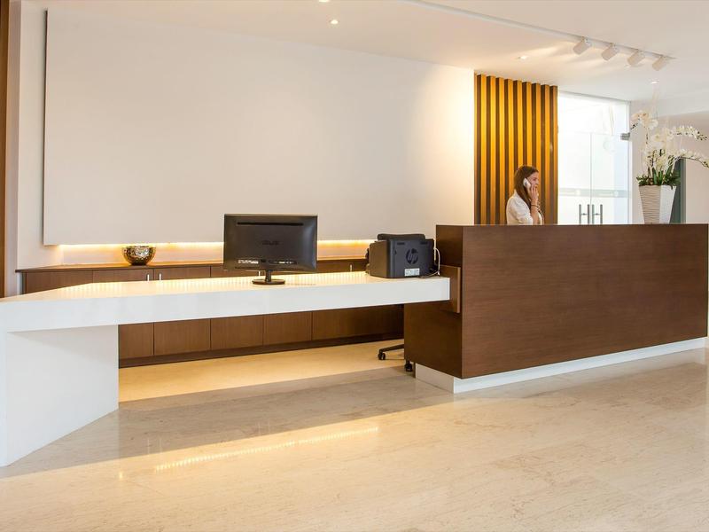 Recepción moderna de hotel con mostrador de madera, computadora y diseño minimalista y claro.