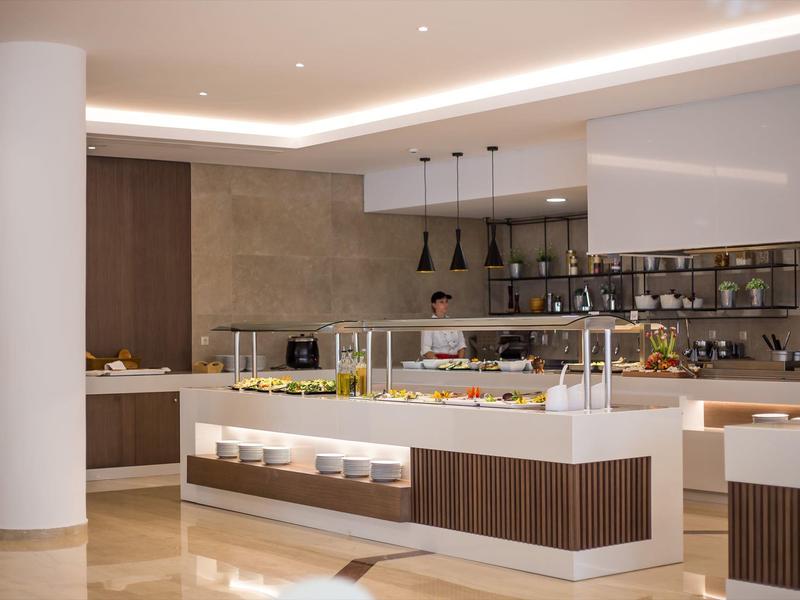Restaurante de hotel moderno con área de buffet, lámparas modernas y combinación de colores blanco y marrón.