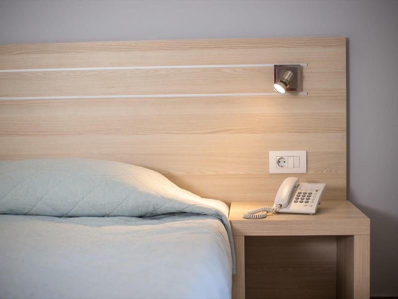 Dormitorio con cama azul claro, cabecero de madera, mesita con teléfono y lámpara.