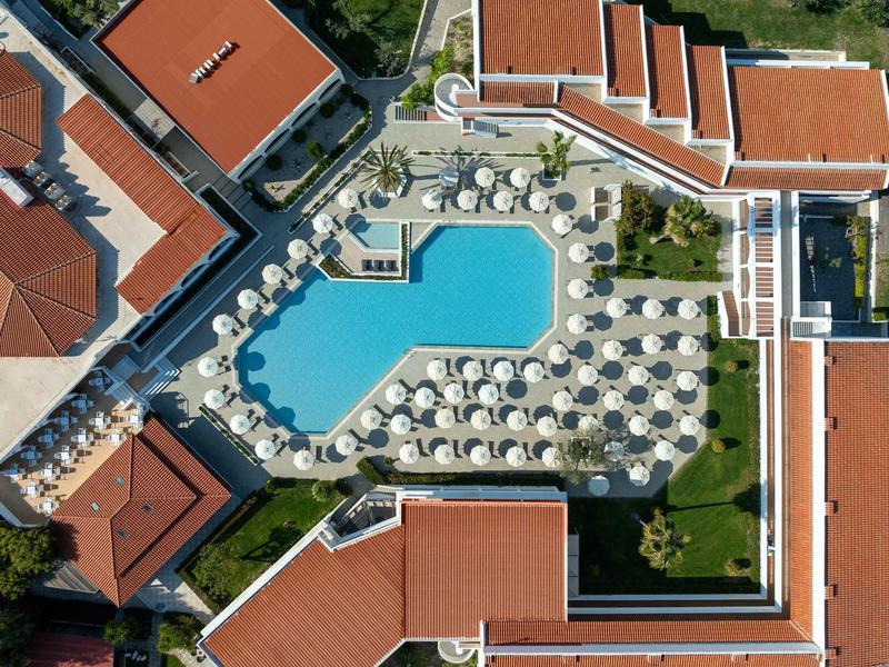 Vista aérea de una piscina con tumbonas y techos rojos en un complejo hotelero.