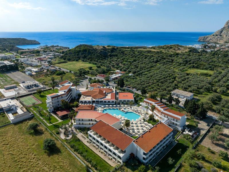 Complejo hotelero con tejados rojos y gran piscina cerca del mar y zonas verdes circundantes.