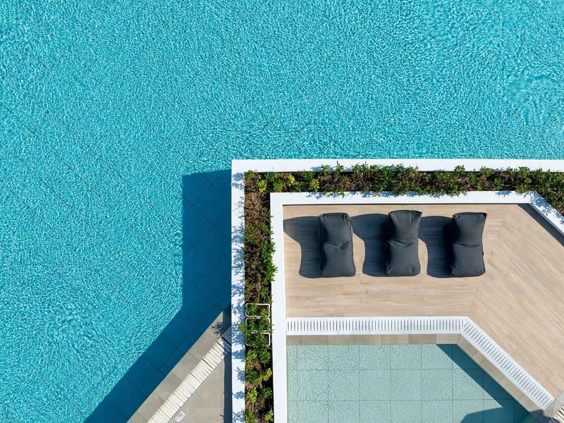 Piscina azul con tres tumbonas negras en una plataforma rodeada de plantas verdes.