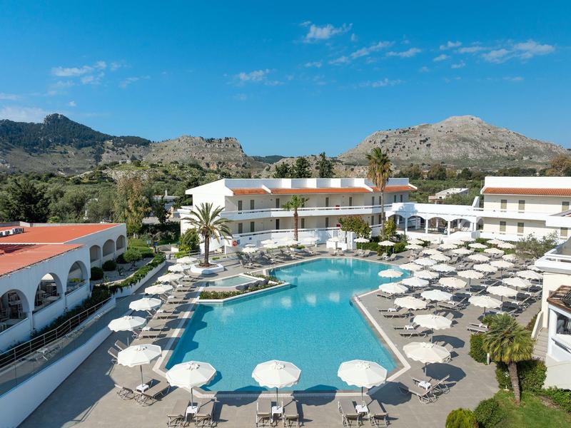 Gran piscina del hotel con sombrillas, tumbonas y edificios blancos alrededor bajo un cielo despejado.