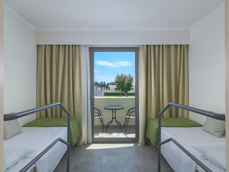 Habitación con dos camas individuales y balcón con vista al exterior en un hotel.