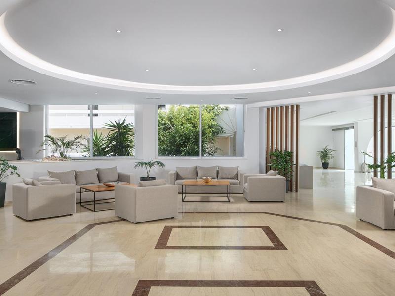 Área de salón luminosa de hotel con sofás modernos, grandes ventanas y elegantes acentos de plantas.