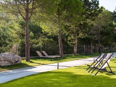 Spokojny ogród z leżakami i parasolami obok zadbanego trawnika i drzew.