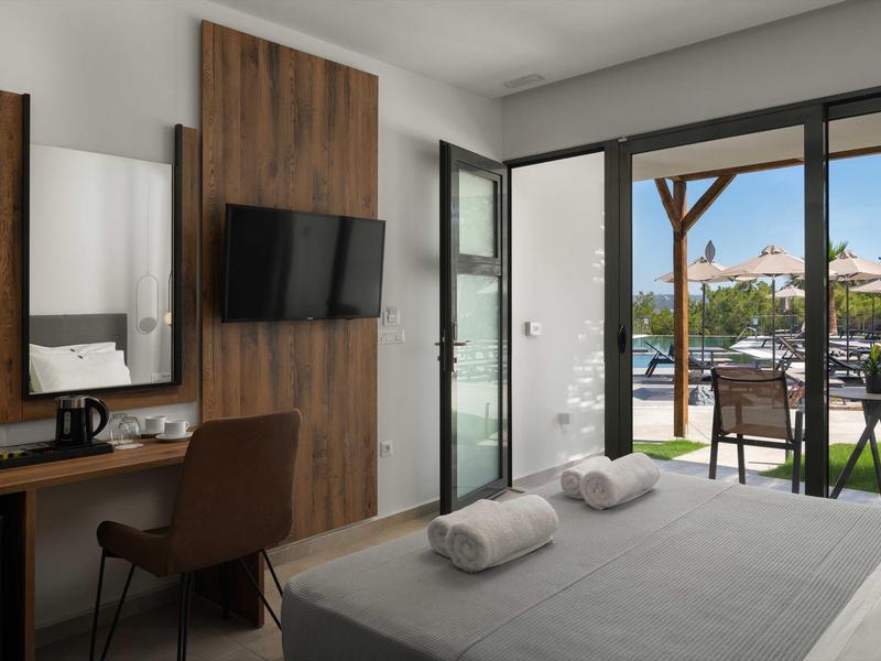 Nowoczesny pokój hotelowy z łóżkiem dwuosobowym, biurkiem, TV i widokiem na basen i taras.