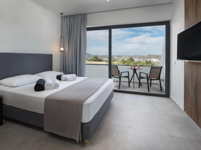 Nowoczesny pokój hotelowy z łóżkiem king-size i balkonem z widokiem na krajobraz.