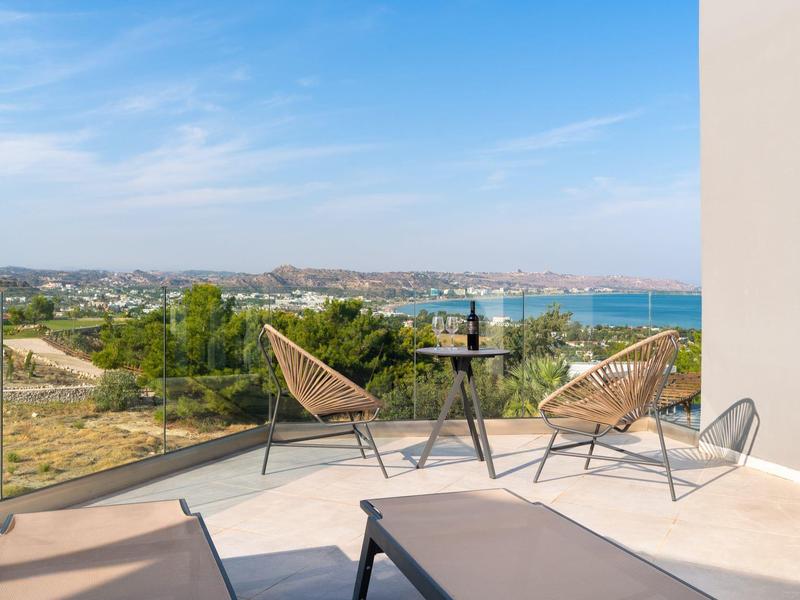 Nowoczesny balkon z krzesłami i stołem z widokiem na zieleń i morze.