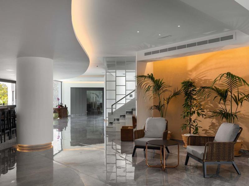 Nowoczesna strefa lounge w hotelu z szarymi fotelami, roślinami i ciepło oświetlonym akcentem ściennym.