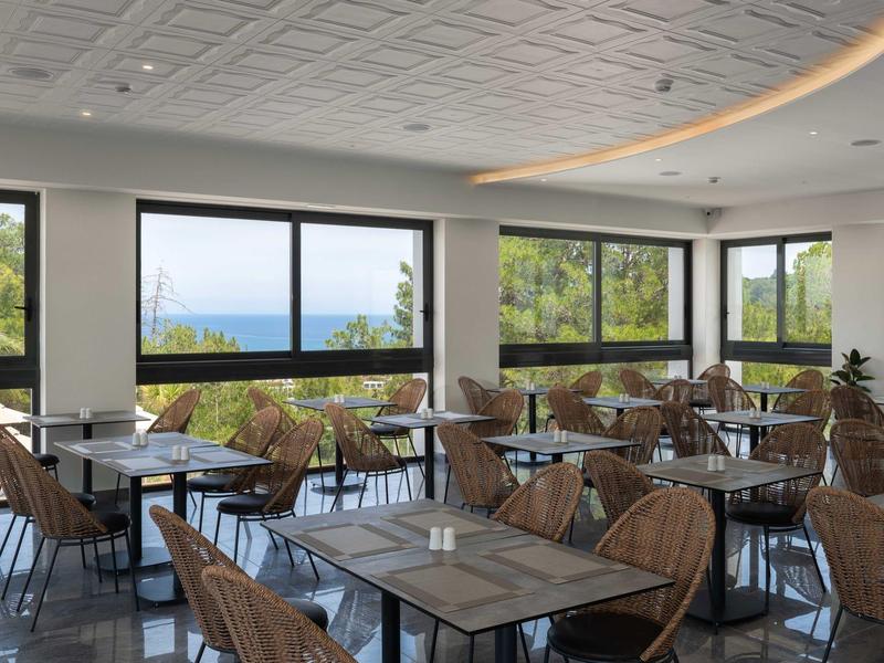 Nowoczesna jadalnia z dużymi oknami z widokiem na morze i otaczającą przyrodę.