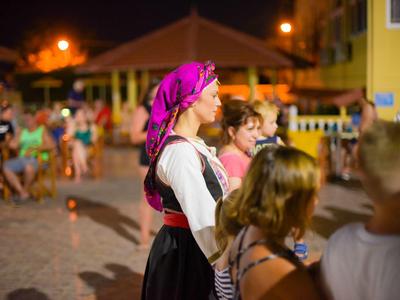 Frau in traditioneller Tracht mit pinkem Kopftuch steht im Nachtmarkt mit Menschen.
