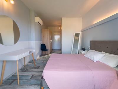 Modernes Schlafzimmer mit rosa Bettdecke, grauem Polsterbett, Spiegel und schlichtem Schreibtisch.