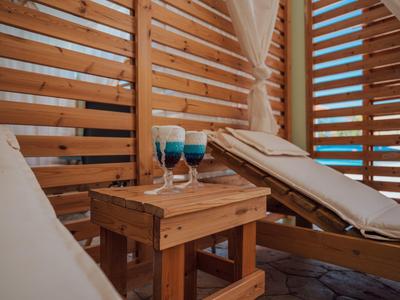 Zwei Liegestühle mit weißen Polstern und Getränke auf kleinem Holztisch in Holzhütte mit Lattenwänden.