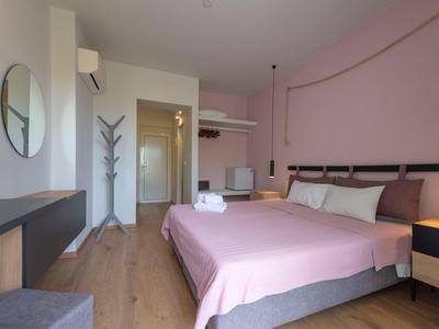 Modernes Schlafzimmer mit rosa Wand und Bett, Holzboden, Spiegel und Garderobenständer in hellem Licht.