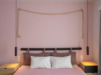Schlichtes Schlafzimmer mit rosa Wänden, Doppelbett, drei Kissen und zwei Nachttischen mit Lampen.
