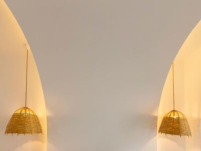 Minimalistisches Schlafzimmer mit weißem Bett, grünem Kissen, goldenen Hängeleuchten und warmem Licht.