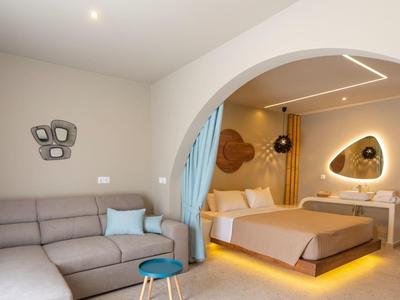 Modern eingerichtetes Schlafzimmer mit Doppelbett, Sofa, sanfter Beleuchtung und blauen Vorhängen.