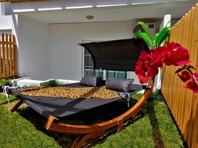 Große schwarze Hängematte mit Holzgestell im Garten, neben einem Zaun und roter Orchidee im Vordergrund.
