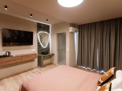 Schlafzimmer mit großem Bett, Wandfernseher, Vorhängen und modernem Spiegel mit Beleuchtung.