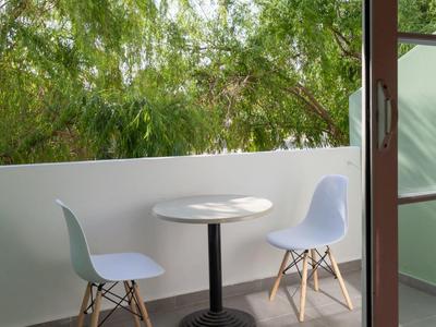 Balkon mit rundem Tisch, zwei weißen Stühlen und grünem Baum im Hintergrund bei Tageslicht.