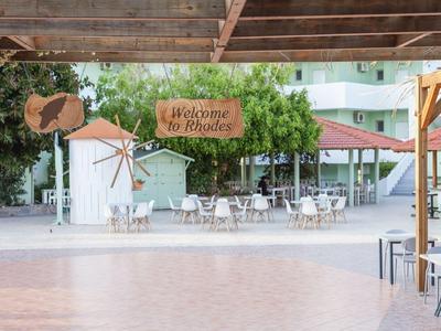 Espace extérieur ouvert avec tables, chaises et panneau 'Welcome to Keratea' sous une pergola en bois.