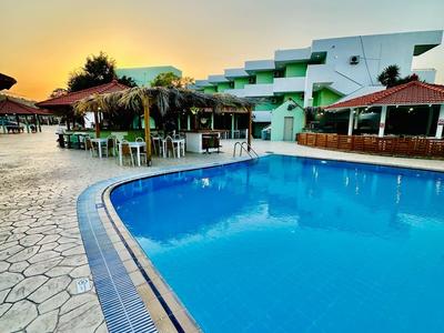 Großer blauer Pool mit umliegender Terrasse und modernen weißen Gebäuden im Sonnenuntergang.