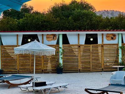Poolbereich mit Liegestühlen, Sonnenschirm und Holzwänden vor einem Gebäude bei Sonnenuntergang.