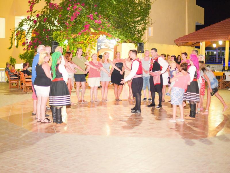 Gruppo di persone che ballano all'aperto di notte, circondati da palme e luci.