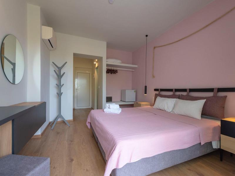 Camera d'albergo moderna con letto matrimoniale, copriletto rosa e pavimento in legno.