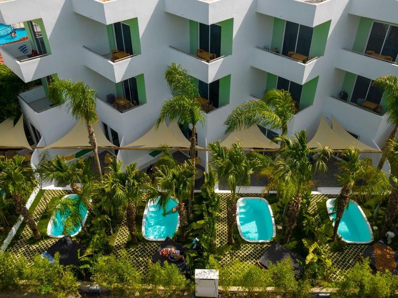 Camere d'hotel moderne con piscine private e palme tropicali all'esterno.