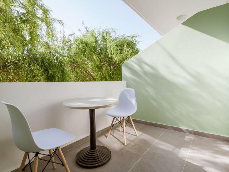 Piccolo balcone con due sedie bianche e un tavolo rotondo, soleggiato con vista verde.