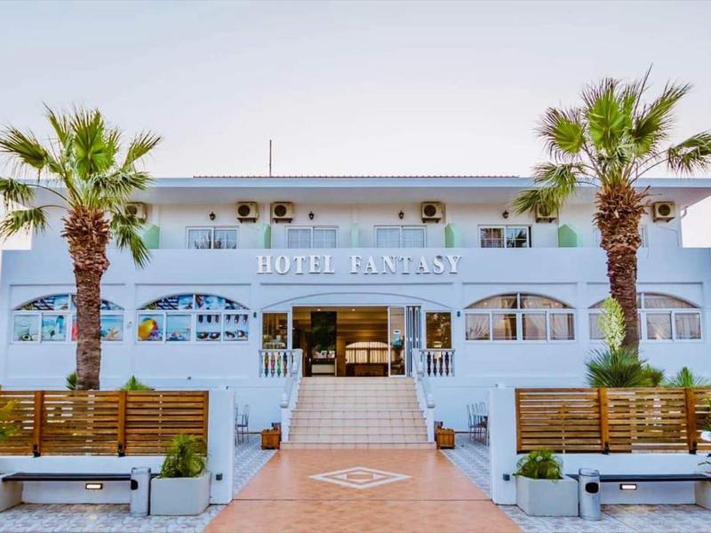Edificio dell'hotel azzurro chiaro con palme e panchine all'ingresso.