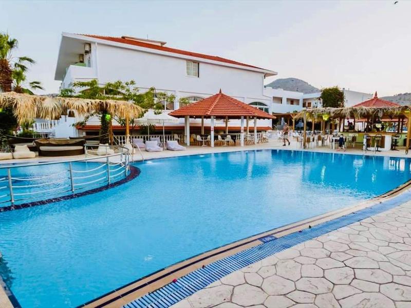 Grande piscina con ombrelloni e lettini davanti agli edifici dell'hotel sotto un cielo blu.