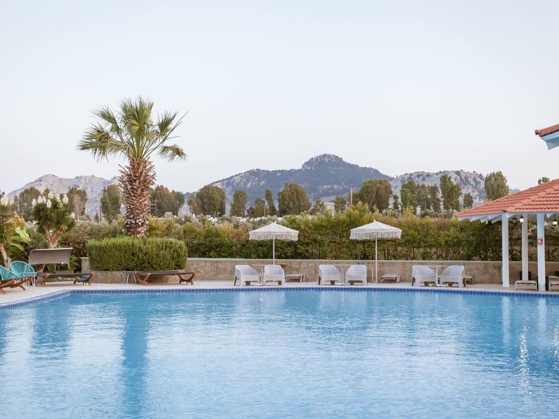 Grande piscina all'aperto con sedie a sdraio ombreggiate e palme davanti a uno sfondo montano.