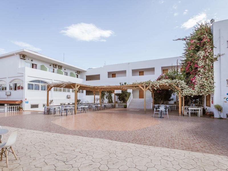 Area terrazza dell'hotel aperta con tavoli e sedie sotto pergolato in una giornata soleggiata.
