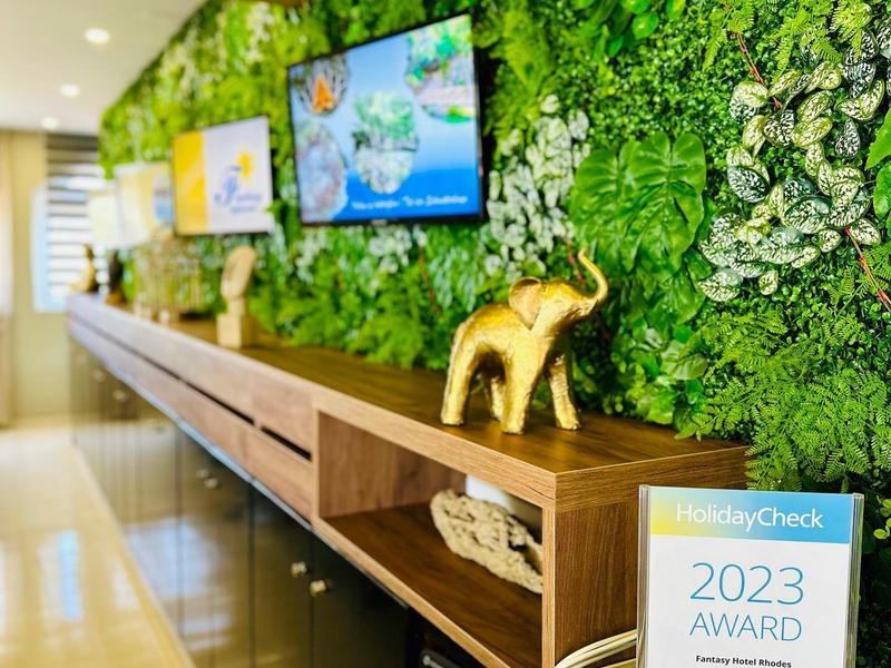 Area reception moderna con parete verde di piante, mensola in legno e premio 2023