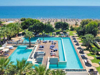 Duży basen na świeżym powietrzu z leżakami i parasolami, palmami i plażą w tle