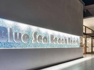 Wejście z podświetlanym napisem „Blue Sea Beach Resort” na nowoczesnej elewacji nocą.
