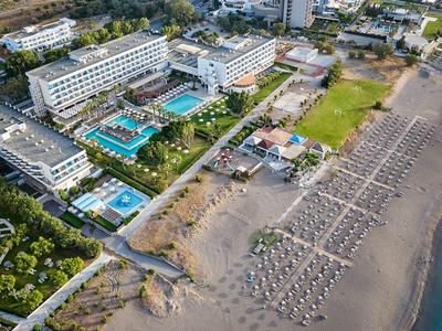 Aerial view of a hotel with several pools and sunbeds on the sandy beach near the sea.