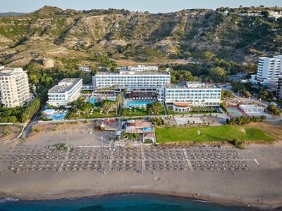 Large beachfront hotel with sun loungers and mountains in the background.
