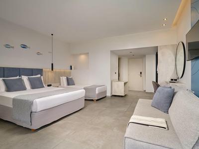 Modern hotel room with large bed, sofa, TV, and minimalist decor.