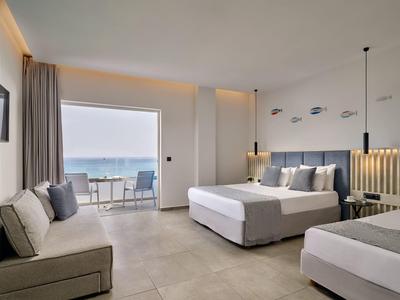Bright hotel room with two beds, sofa, and balcony view of the sea