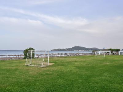 Zielona trawa z bramkami do piłki nożnej na tle plaży i morza pod pochmurnym niebem.