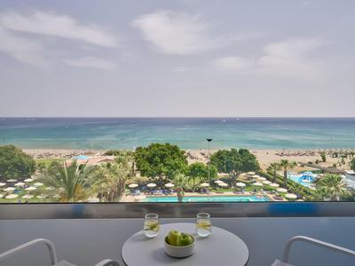 View from balcony overlooking pool, palm trees, and ocean under cloudy sky.